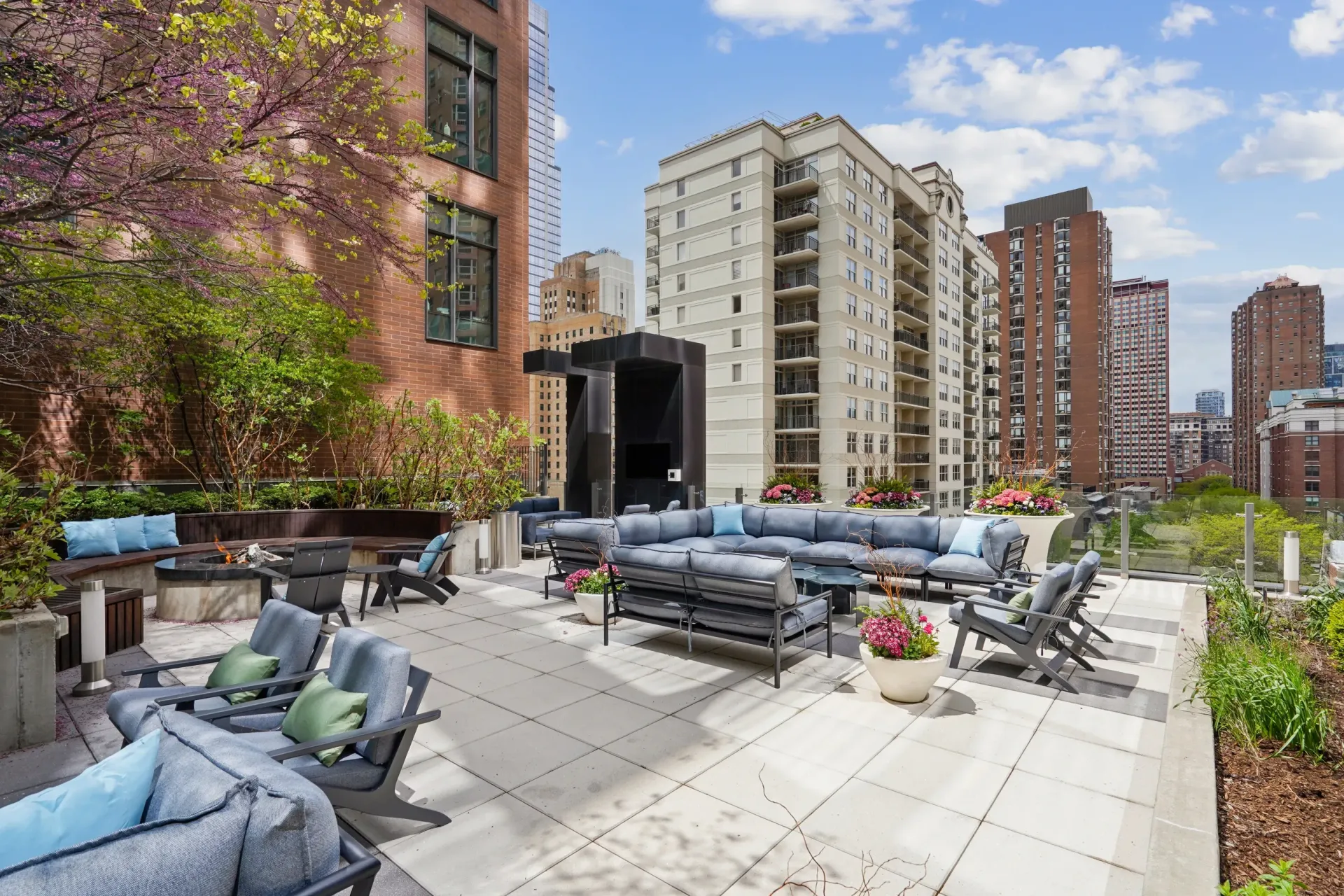 Rooftop patio with lounge seating, potted plants, and city apartment buildings in the background