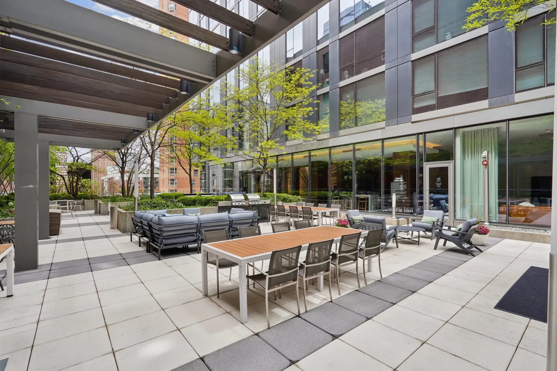 Modern courtyard with outdoor dining tables, black chairs, trees, and apartment building balconies