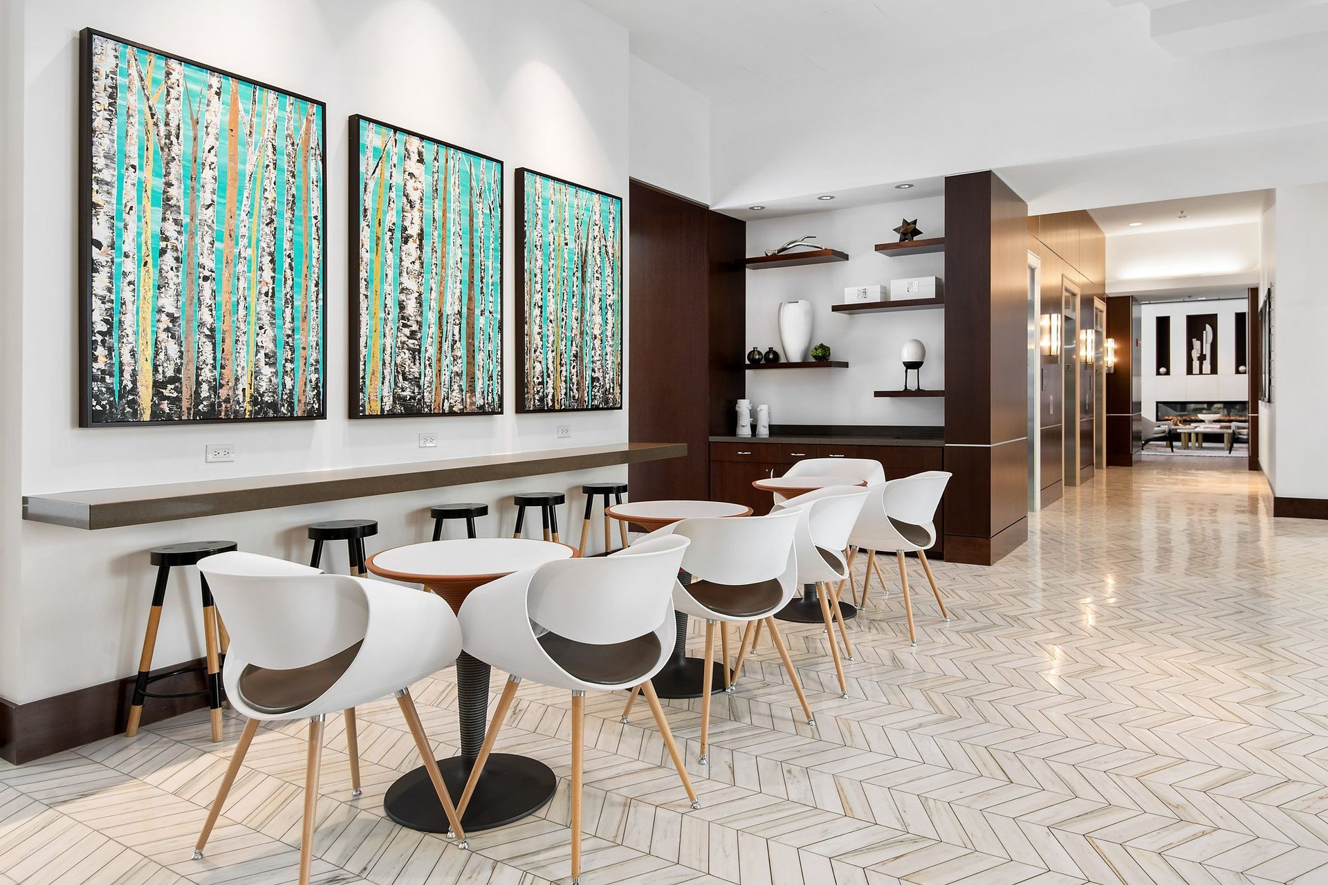 a dining room with white chairs and a bar with three paintings on the wall