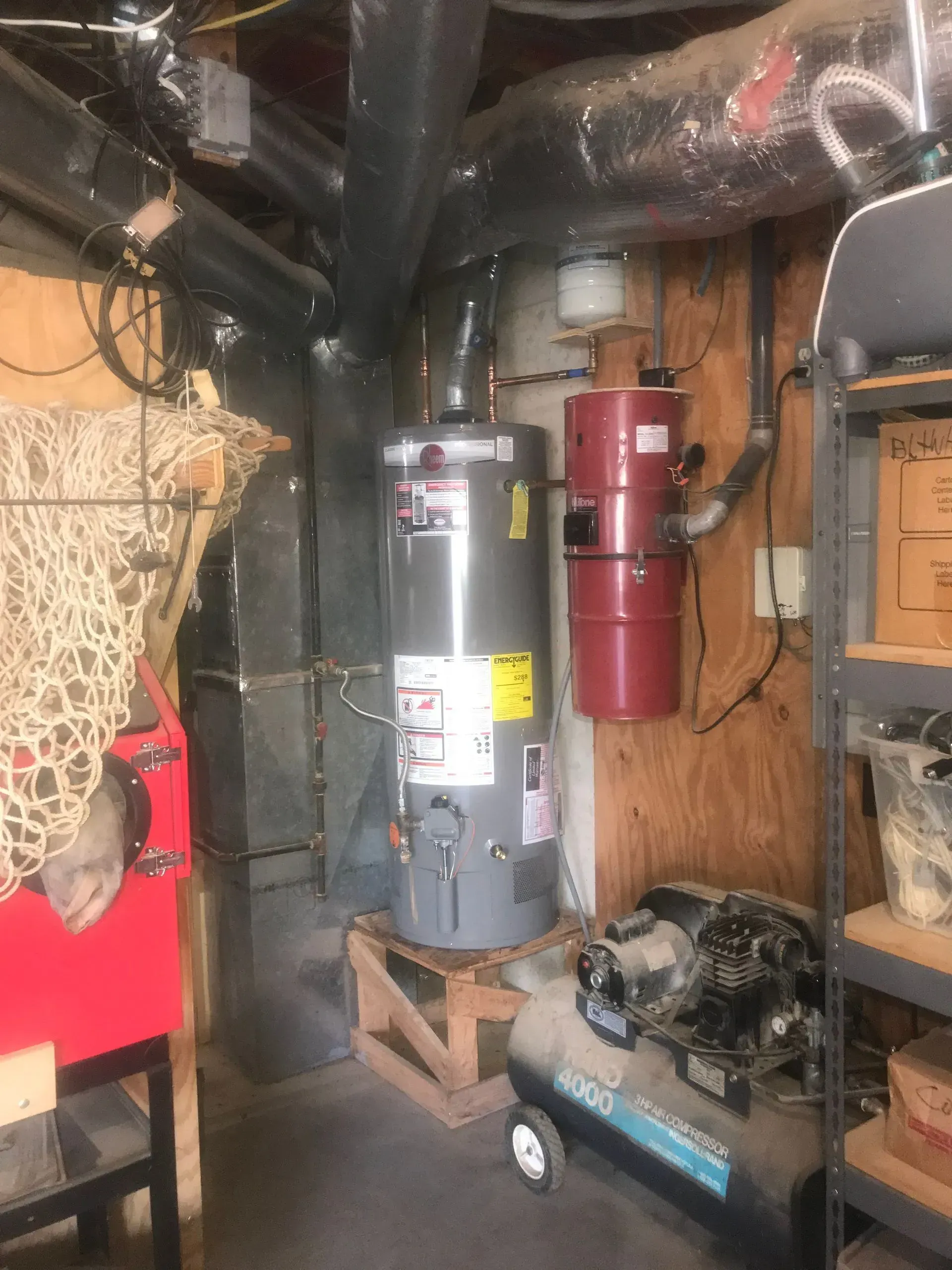 Water heater and central vacuum system in a basement utility area; gray, red, and brown tones.