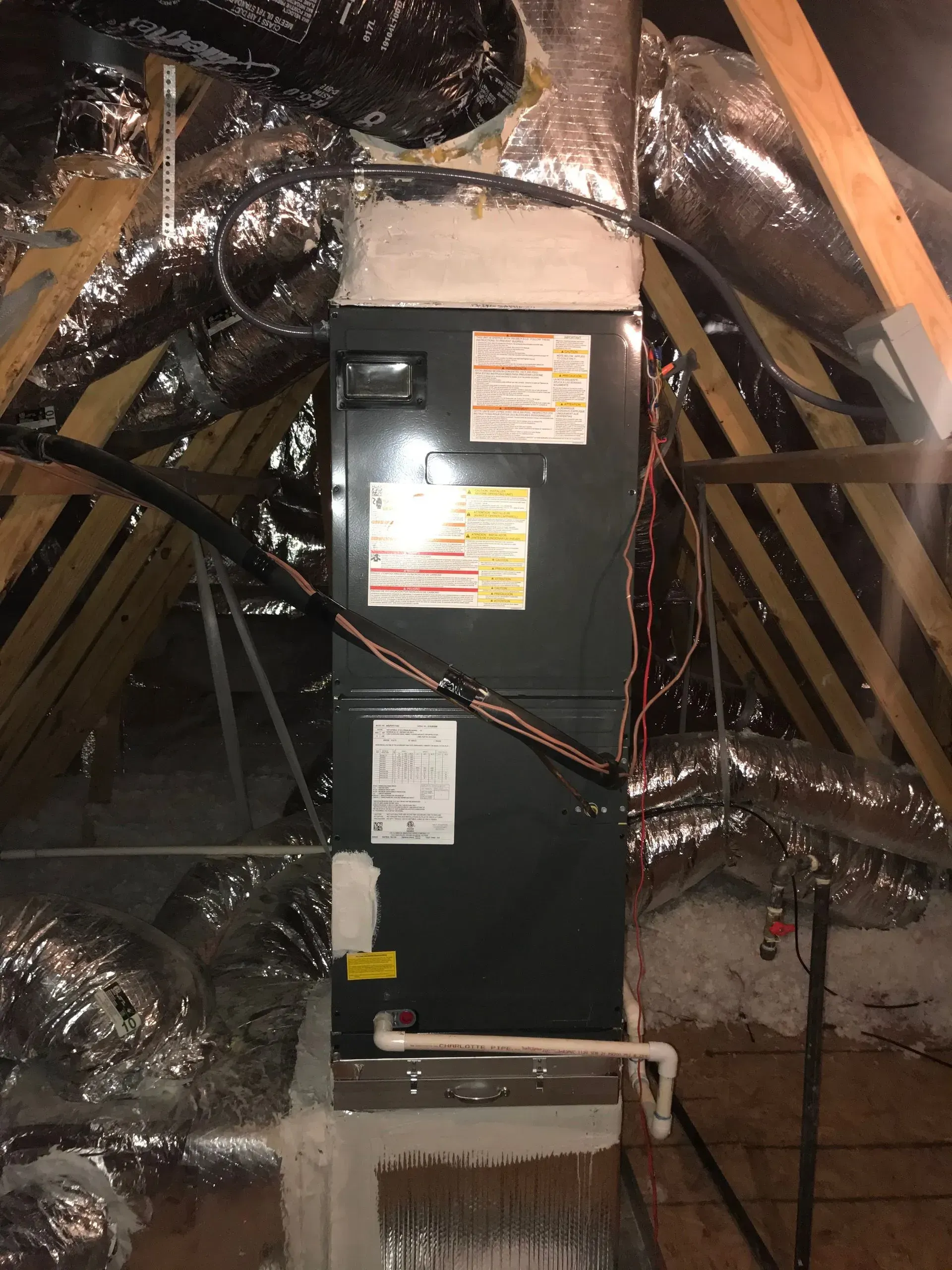 HVAC unit in a residential attic, surrounded by ductwork and wooden beams.