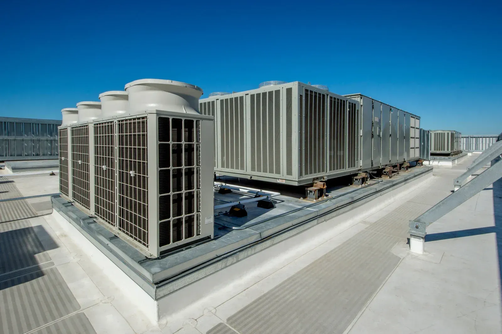 Rooftop HVAC units against a clear, blue sky. Grey and white units on a flat roof.
