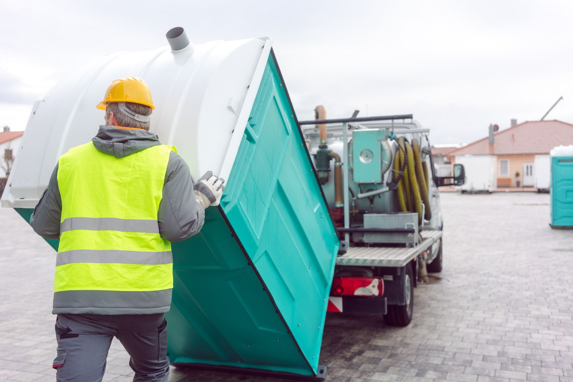 Worker in safety vest moving a portable toilet beside a service truck. Worker in safety vest moving a portable toilet beside a service truck.