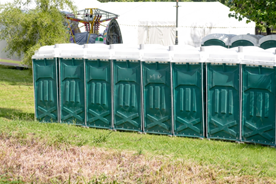 Row of green portable toilets at outdoor festival event on grass.