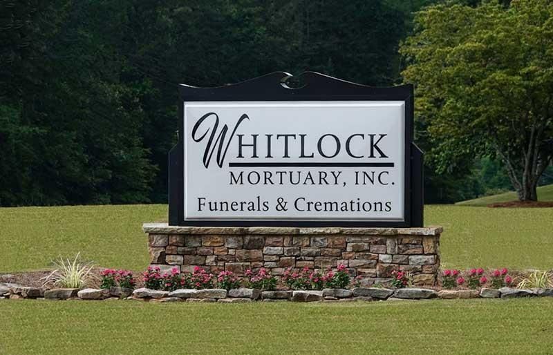 Whitsock Mortuary Inc. sign on a stone base in front of a grassy lawn and trees