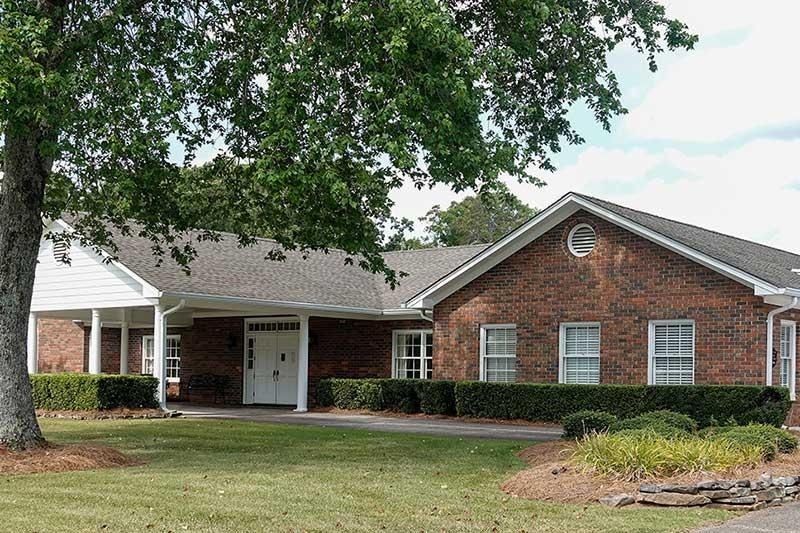 Brick house with white porch and garage, partly shaded by a large tree in a suburban yard