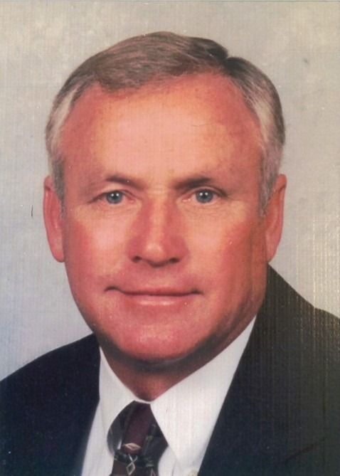 Studio portrait of a man in a dark suit and tie, facing forward with a neutral expression.