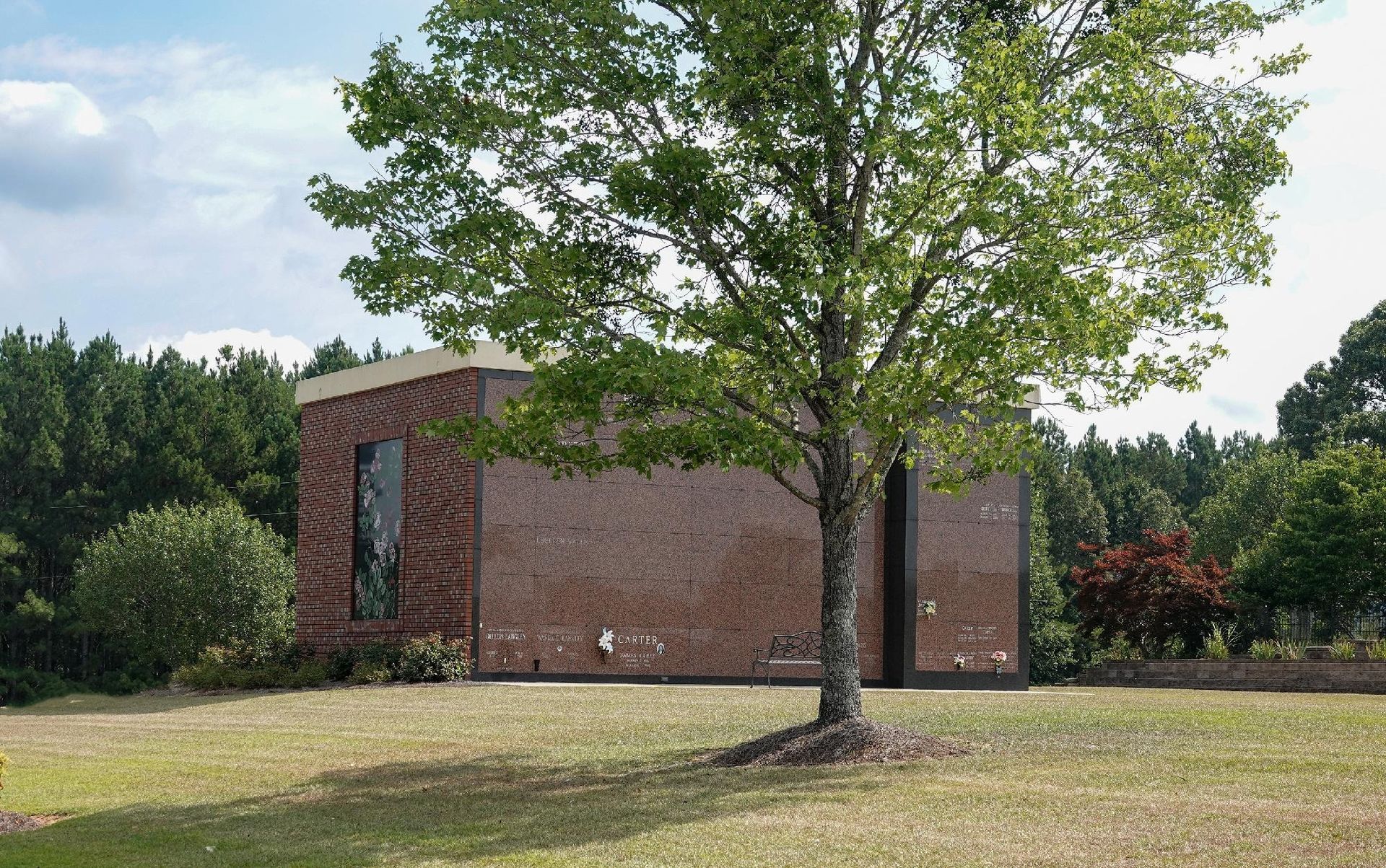 Brick building behind a leafy tree in a grassy park-like setting under a partly cloudy sky