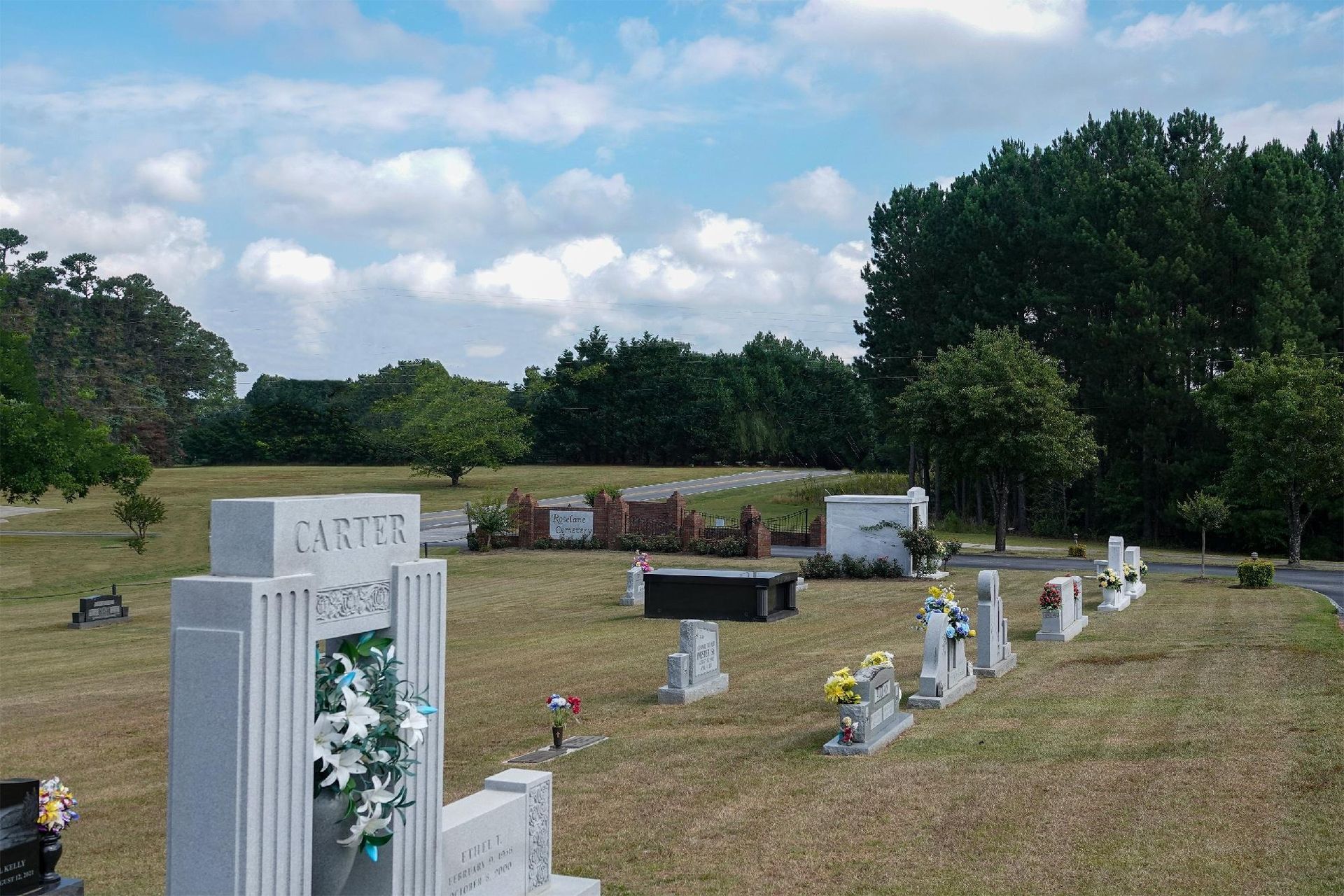 Graveyard with white headstones and flower arrangements under a blue, partly cloudy sky