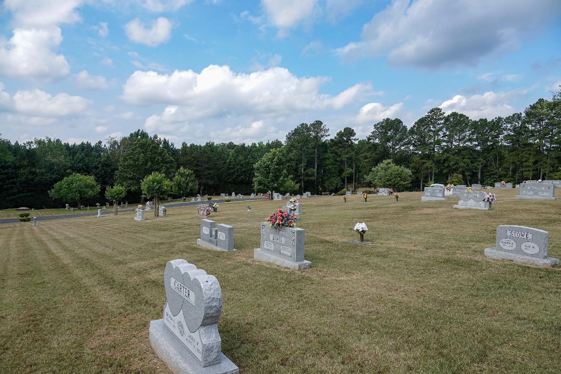 Rows of gravestones in a grassy cemetery under a blue sky with clouds