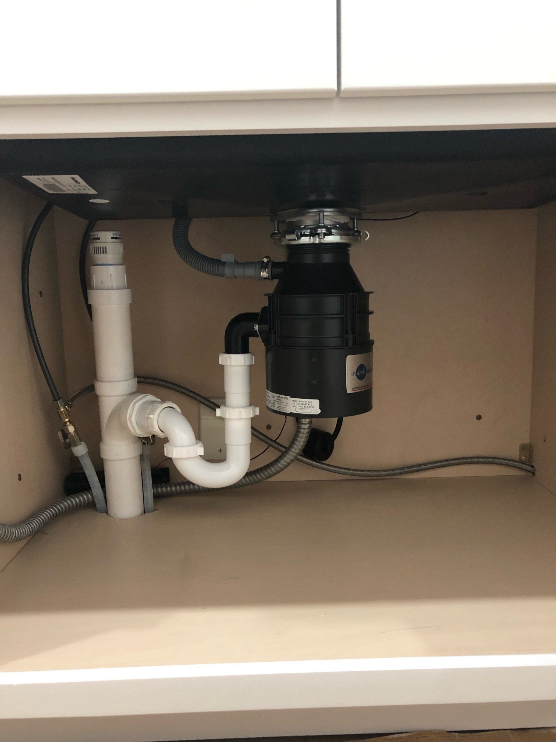Undersink plumbing with garbage disposal. White pipes, a black disposal, and a gray braided hose.