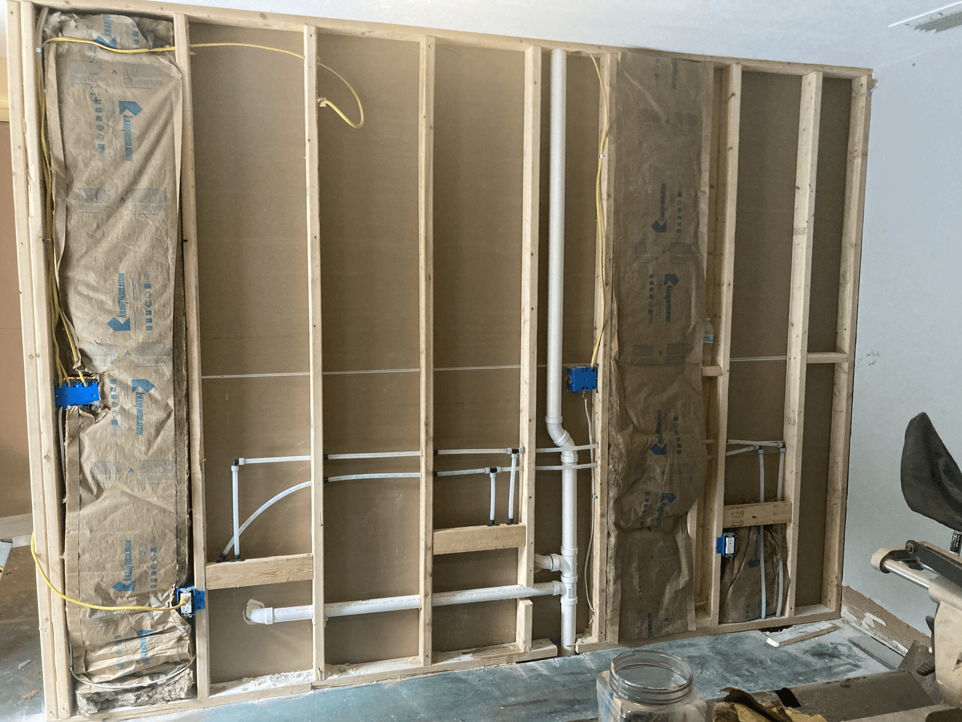 Wooden wall frame with plumbing, electrical wiring, and insulation visible.