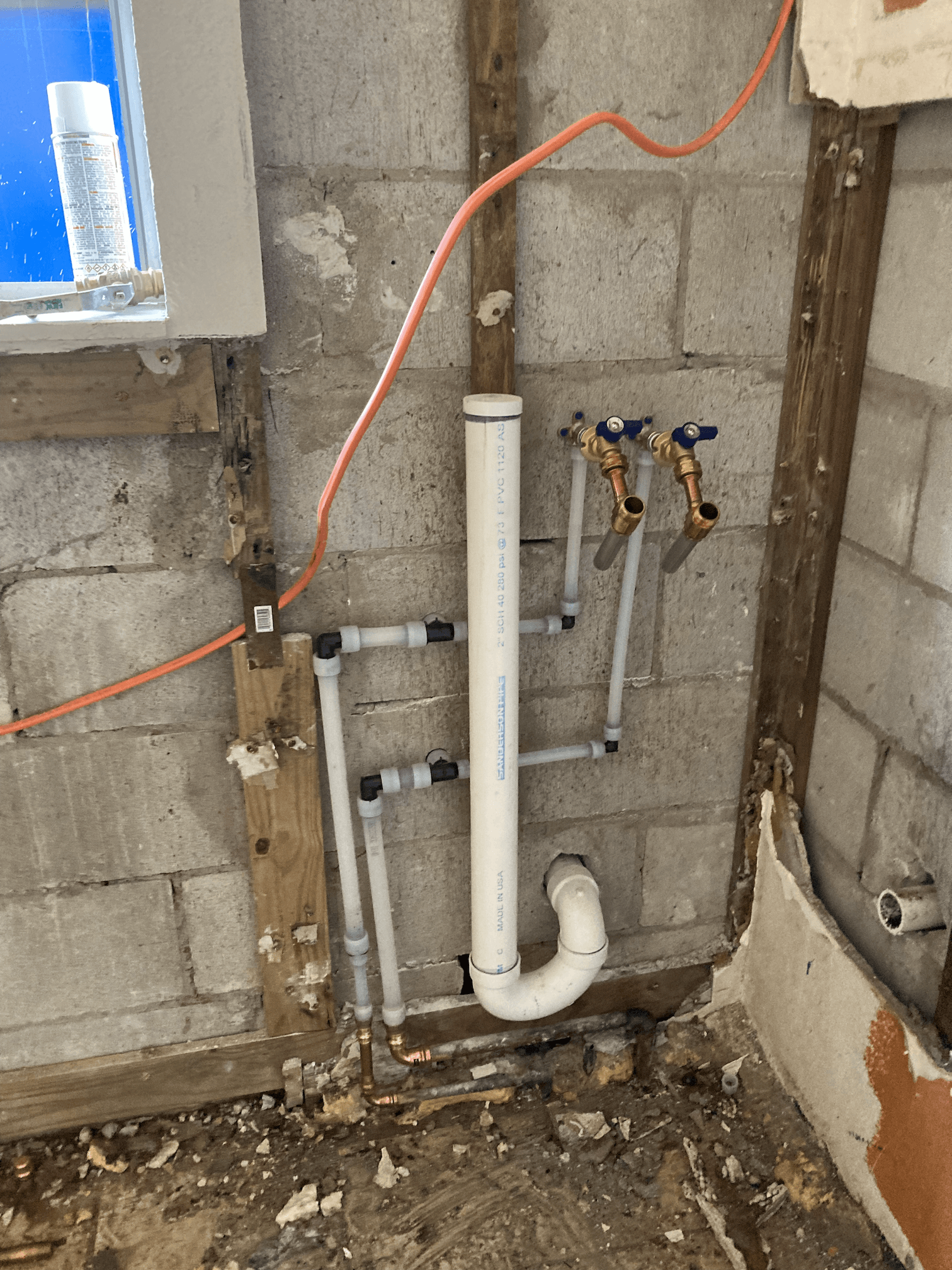 Plumbing pipes and faucets installed on a cinder block wall, with electrical wiring and wood framing.