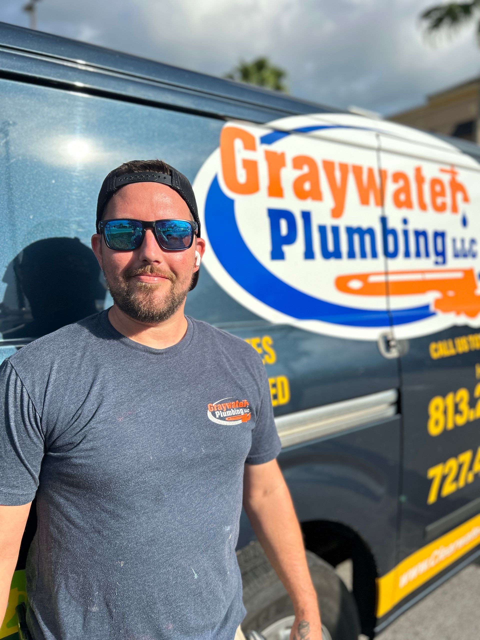 John - Safety Harbor, FL - Graywater Plumbing Man wearing sunglasses stands in front of a Graywater Plumbing van, smiling.