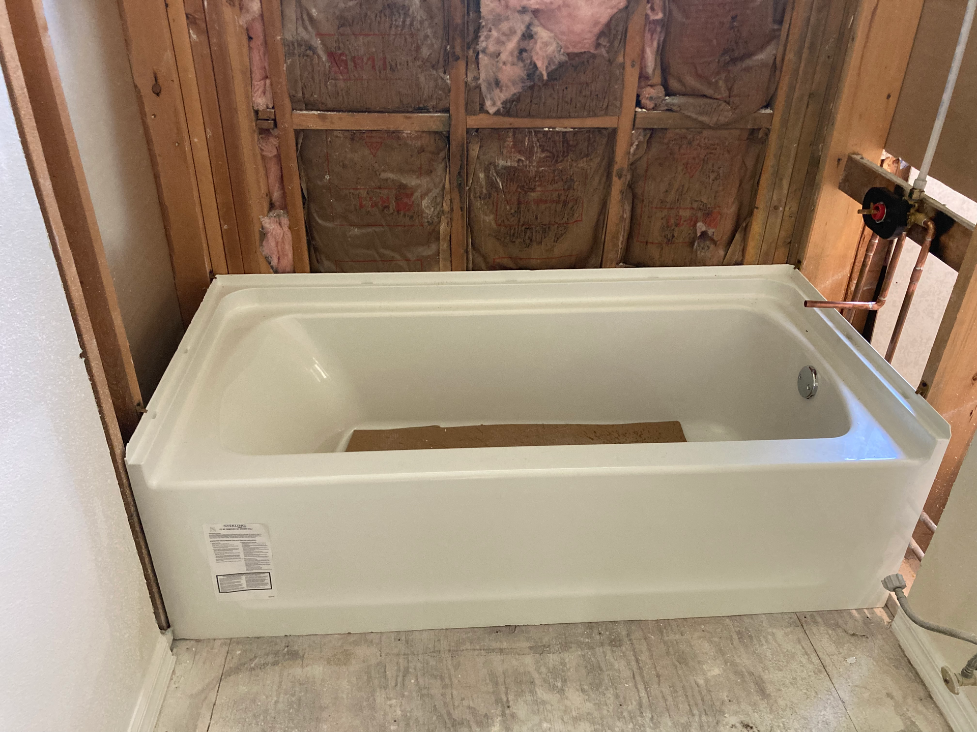 White bathtub installed in a framed-out bathroom. Insulation and exposed plumbing visible.