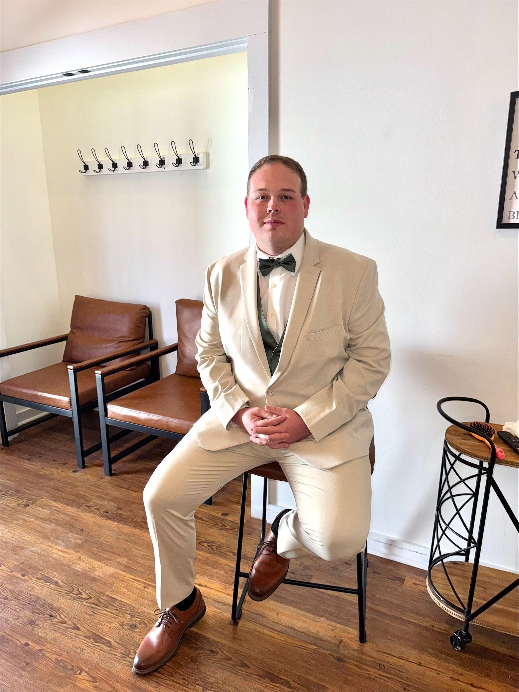 Man in a cream suit seated on a stool in a bright room with wooden floors and minimalist decor