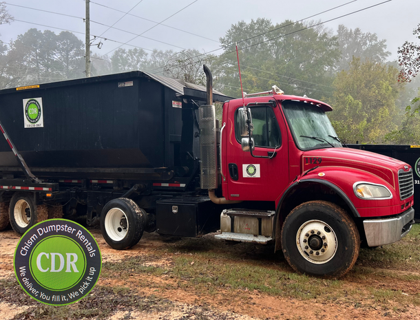 Red dump truck with black trailer parked on a muddy road in a foggy wooded area