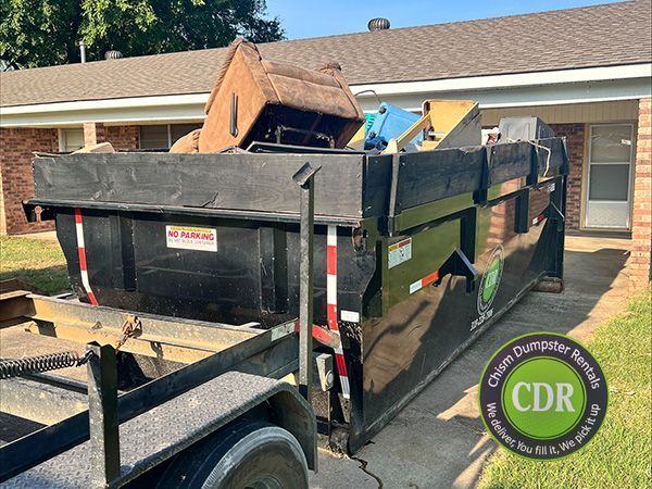 Black dumpster trailer filled with debris parked beside a house in a driveway