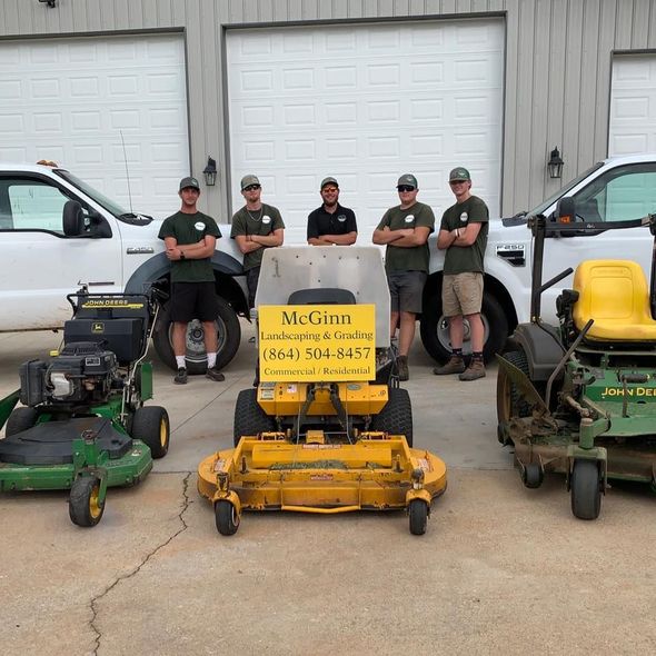 Landscaping crew posing with lawn mowers and trucks in front of a building.