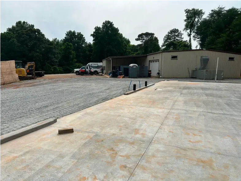 Gravel and concrete lot with a building and equipment. A cloudy sky is overhead.