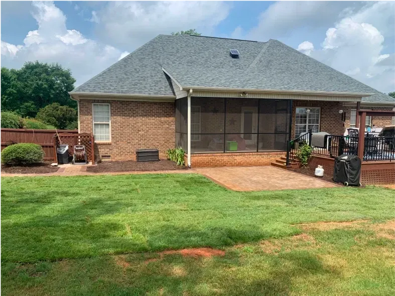 Backyard view of brick house with a screened porch, surrounded by green lawn and a wooden deck.