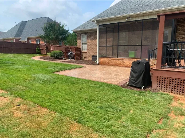 Lush green lawn and paved patio beside a house with a screened porch and wooden deck.