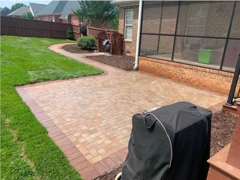 Backyard patio with brick pavers, surrounded by grass and a walkway.