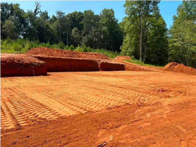 Cleared red dirt lot with tiered berms and tree-lined background.