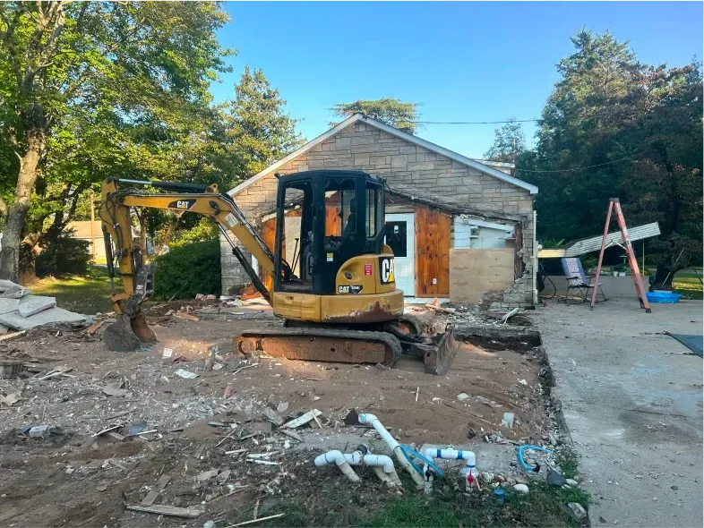 Yellow excavator demolishing a stone building, debris on the ground.