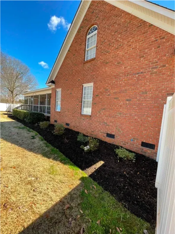 Red brick house with a newly mulched bed and green lawn. Blue sky.