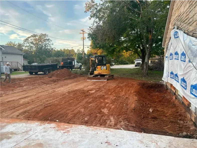 Construction site with excavator and dump trucks; dirt pile near a building under construction.