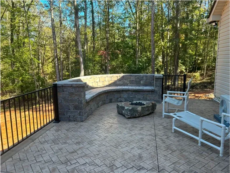Patio with stone bench, fire pit, and metal railing overlooking a wooded area.