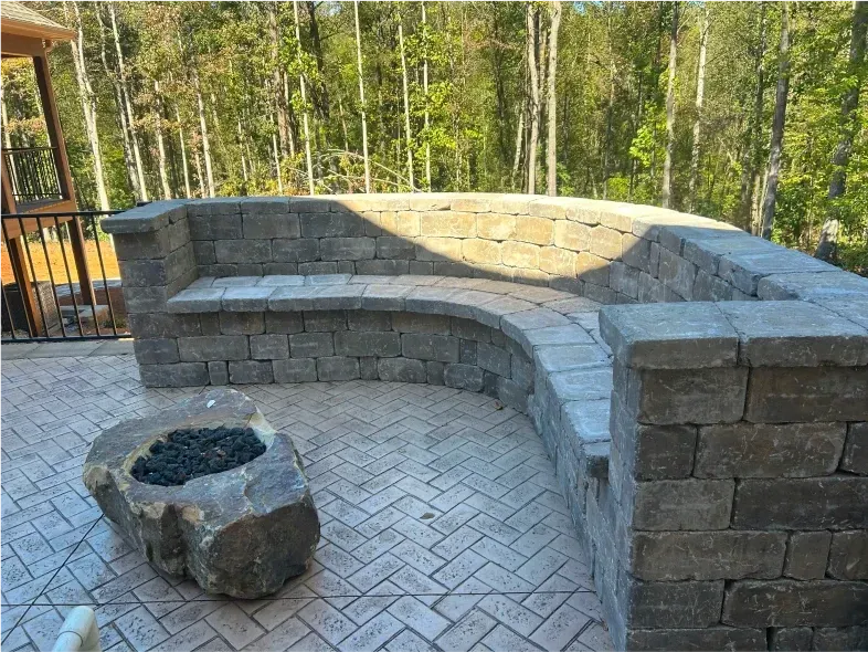 Stone bench with built-in fire pit on a patio, surrounded by trees.