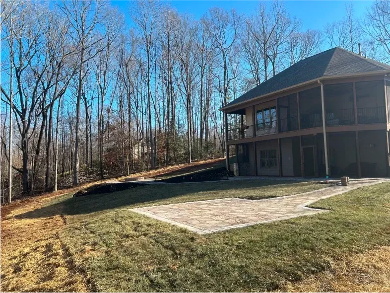House with screened porch, stone patio, and grassy yard near a wooded area.