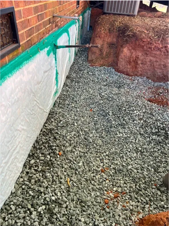 Exterior foundation with gravel drainage, brick wall, and green membrane.