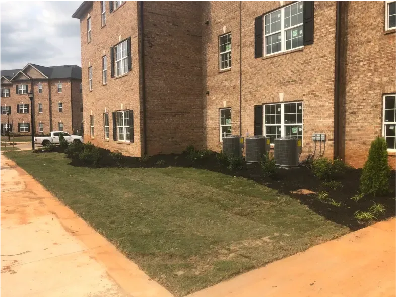 Exterior of brick apartment building with landscaped lawn and black mulch.
