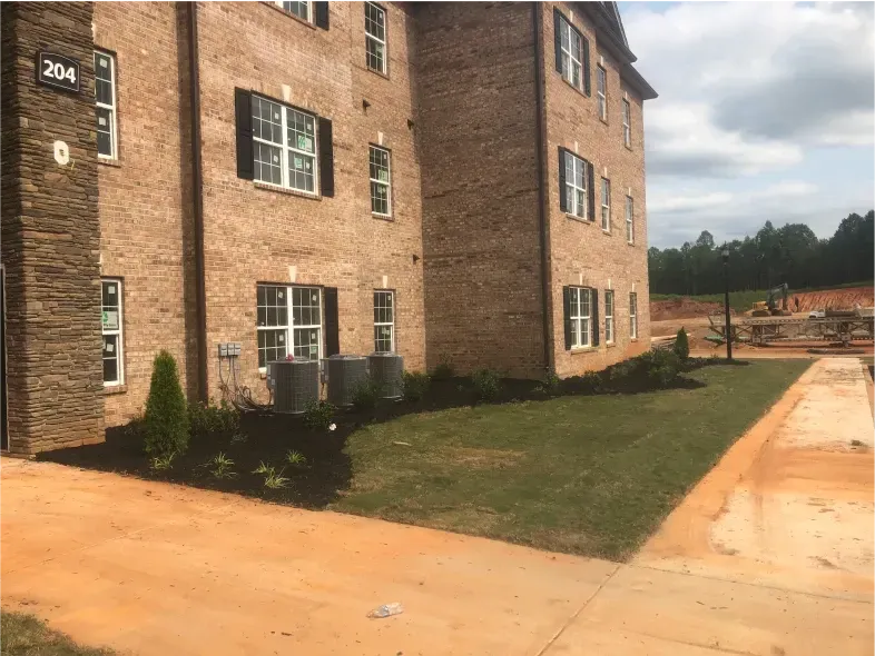 Brick apartment building with black shutters, green grass, and sidewalk.