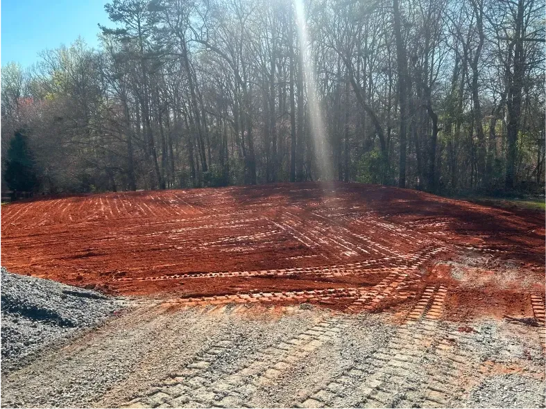 Red dirt hillside cleared for construction, with tire tracks and treeline in the background.