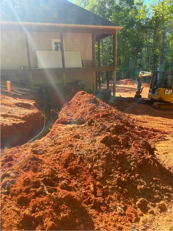 Construction site with house, red dirt, and an excavator.