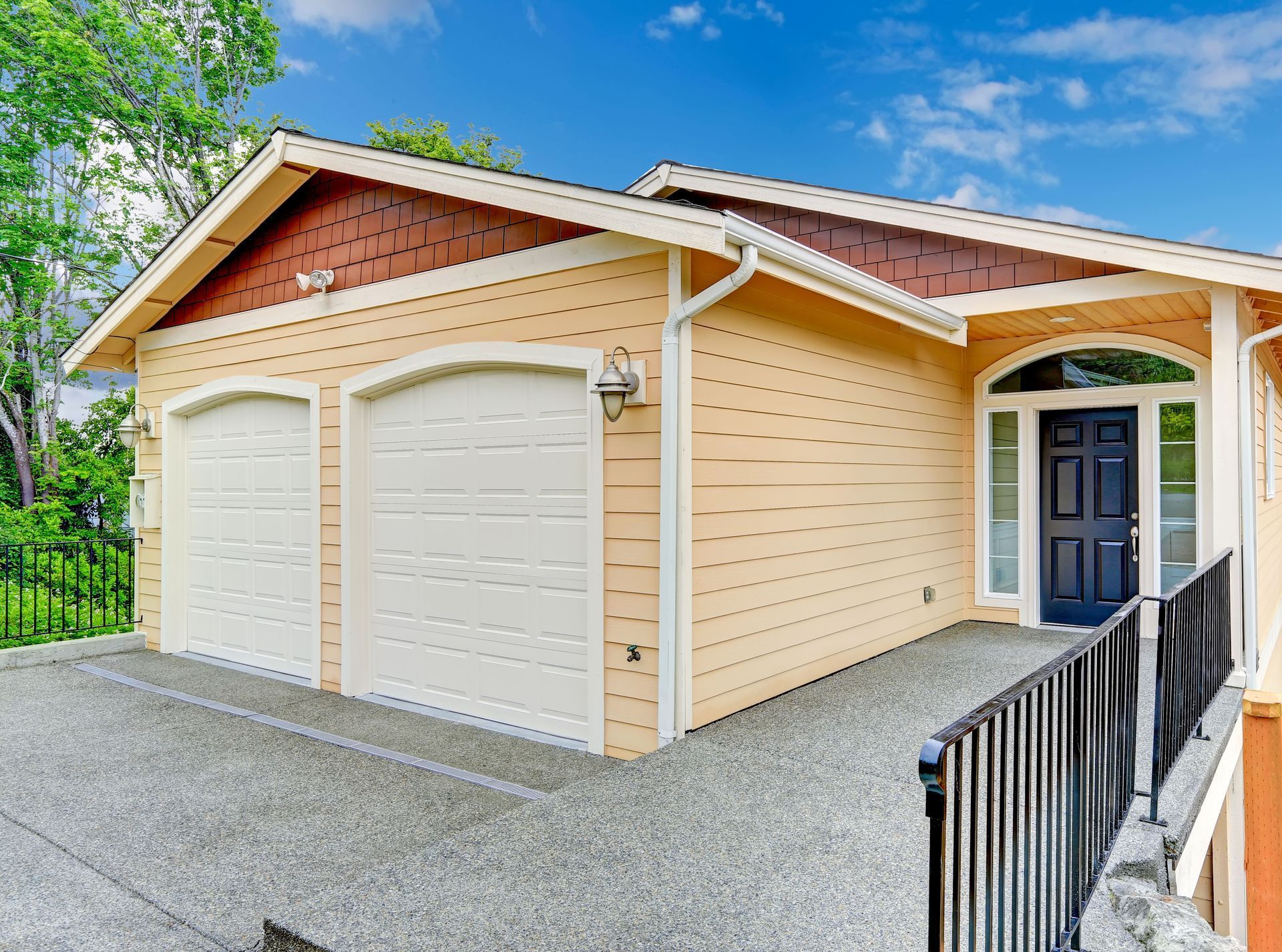 Two-car garage with white doors, beige siding, and a dark front door on a gravel driveway