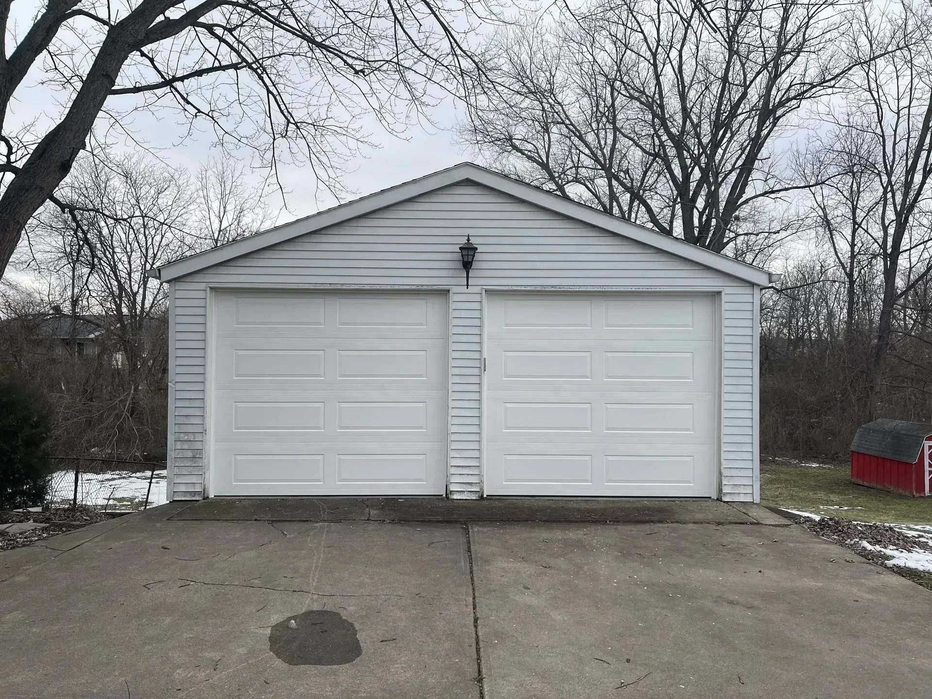 White two-car garage with two closed doors and a concrete driveway in a leafless yard