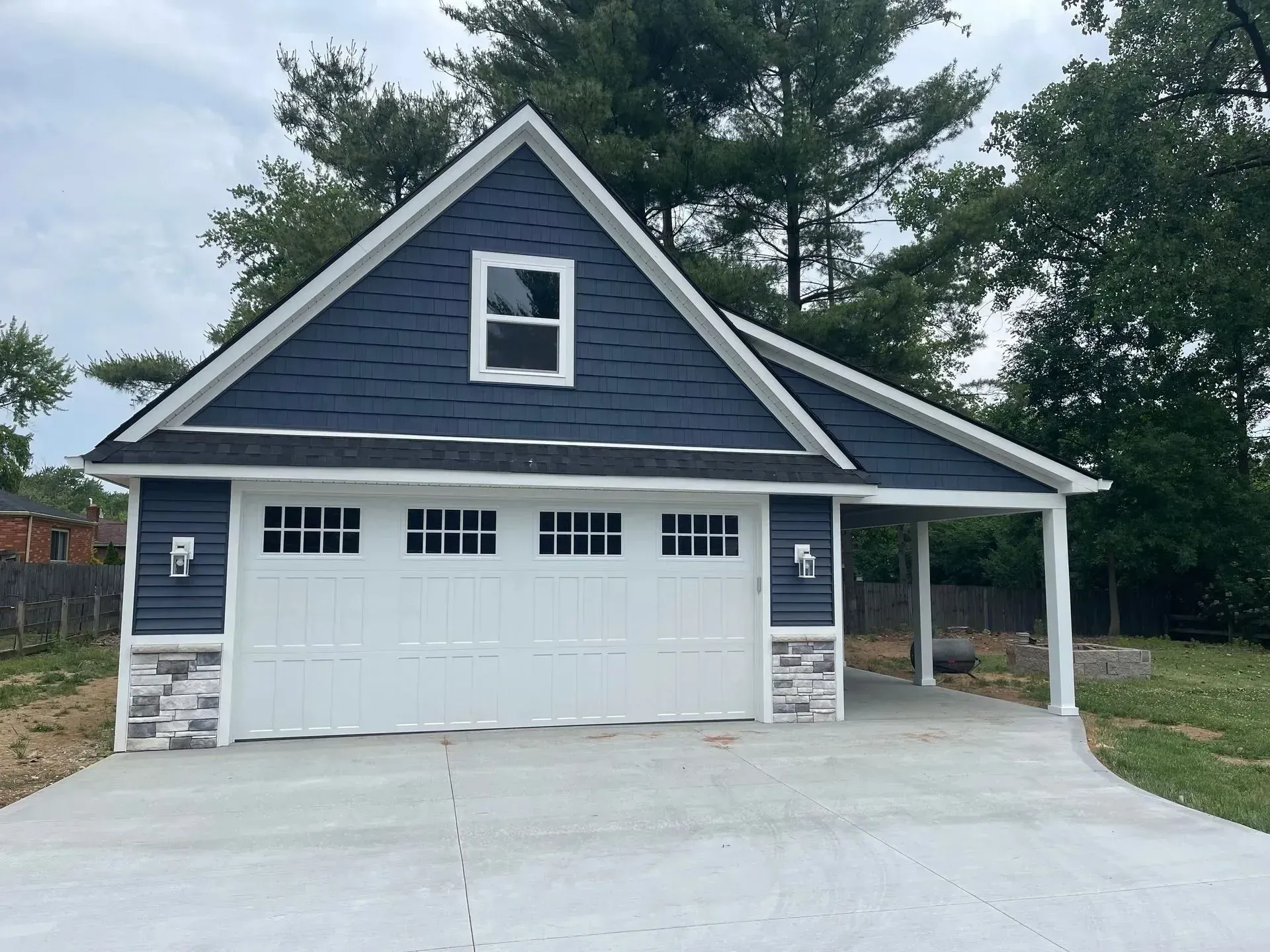 Blue house with white garage doors, stone accents, and a covered side porch