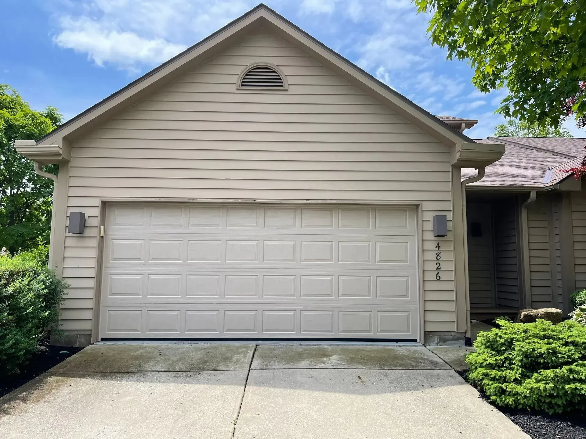 Suburban beige house exterior with a two-car garage and driveway under a blue sky
