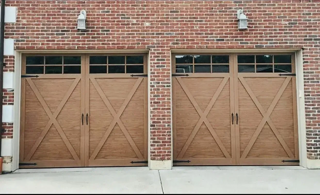 Two wooden garage doors on a red brick building, each with diagonal X-pattern panels and small lights above.