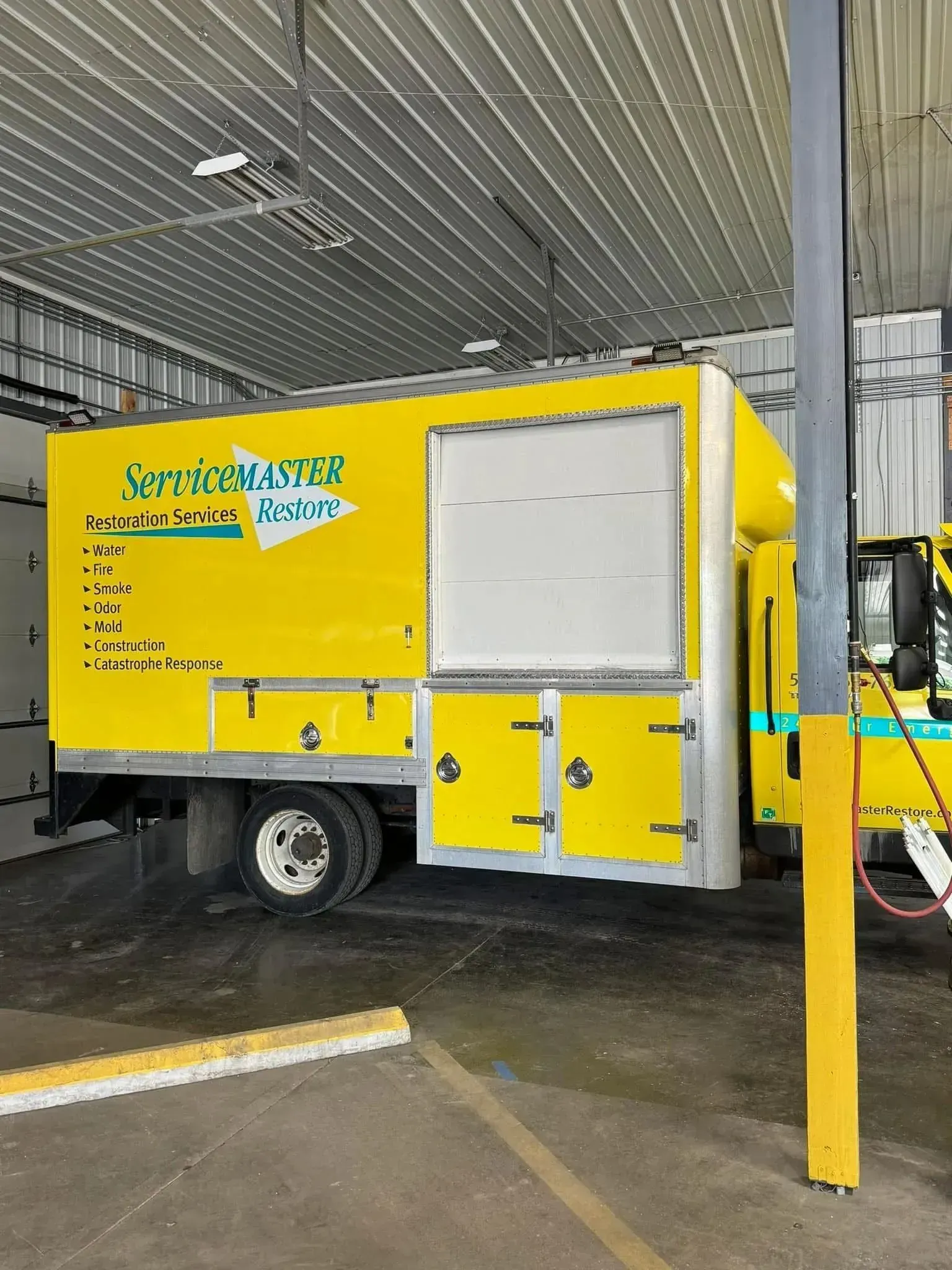 Yellow service trailer parked under a covered area with white panels and a yellow post in front
