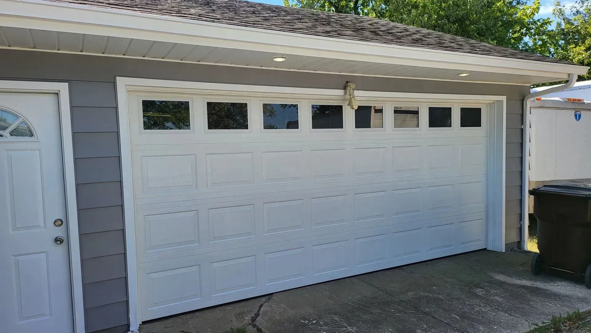 White two-car garage door with small windows, attached to a house in a sunny driveway