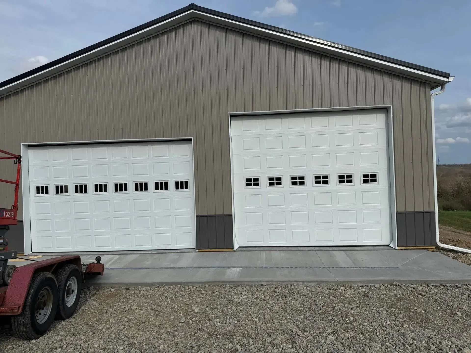 Gray metal garage with two white roll-up doors and gravel driveway