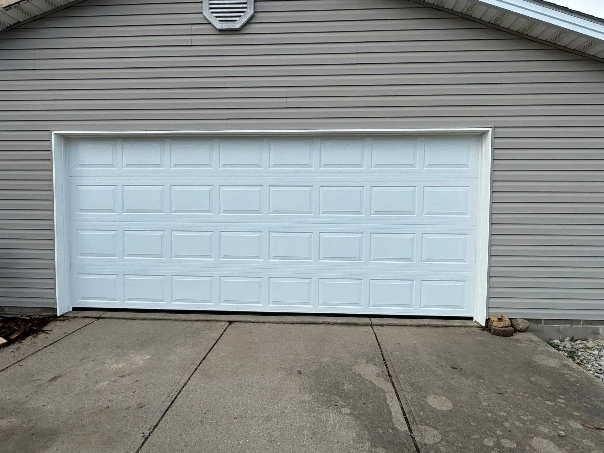 White garage door on a gray-sided house with a concrete driveway in front.