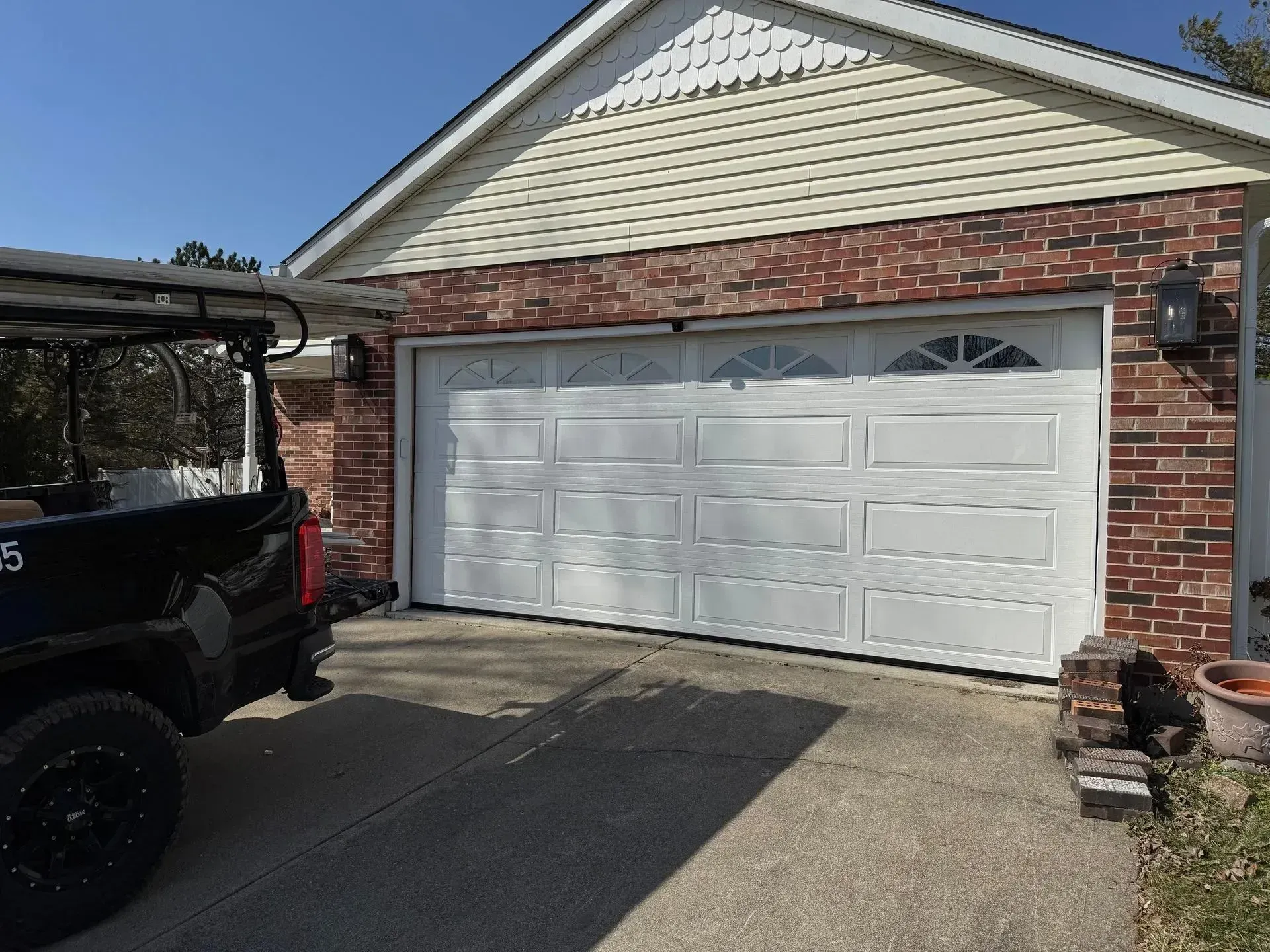 Brick house garage with white double doors and a black vehicle parked on the left side of the driveway