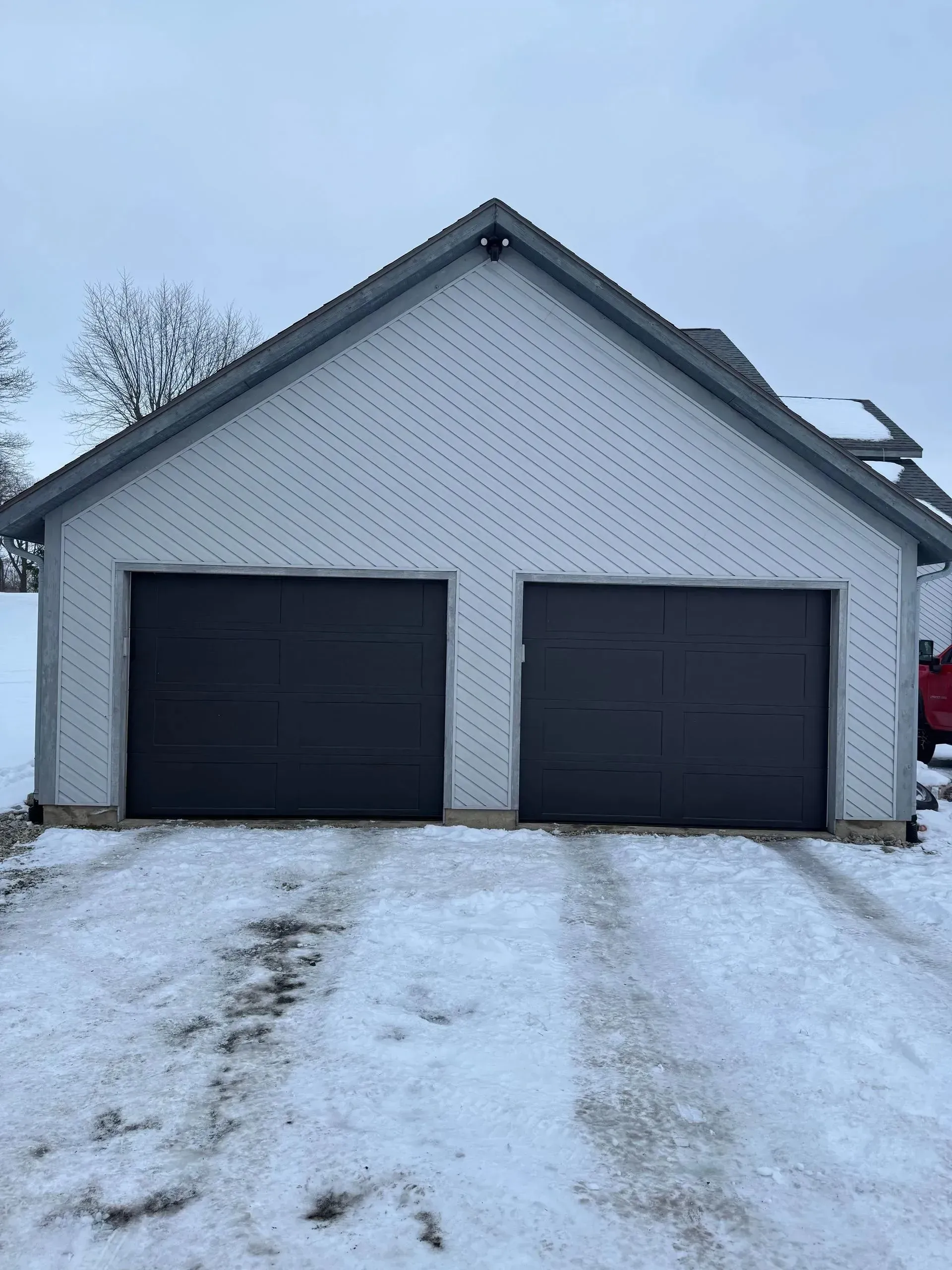 Snow-covered driveway leading to a white two-car garage with dark doors